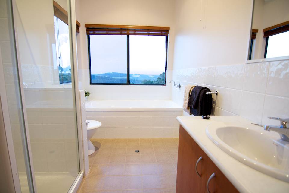 The bright white bathroom of the Karri chalet with shower, bath, basin and toilet.