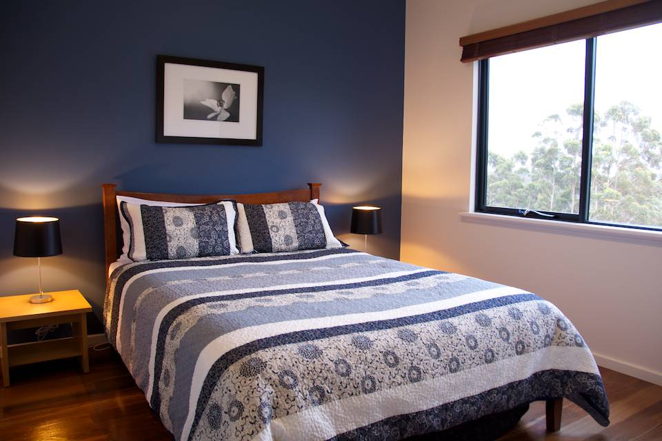 The bedroom in the Karri chalet with side lamps, a double bed and large window looking out to huge trees.