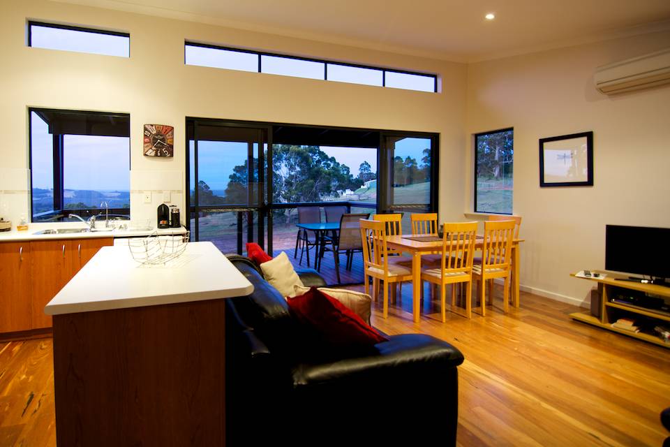 The lounge and dining area of the Karri chalet with wooden table and chairs and black leather couches.