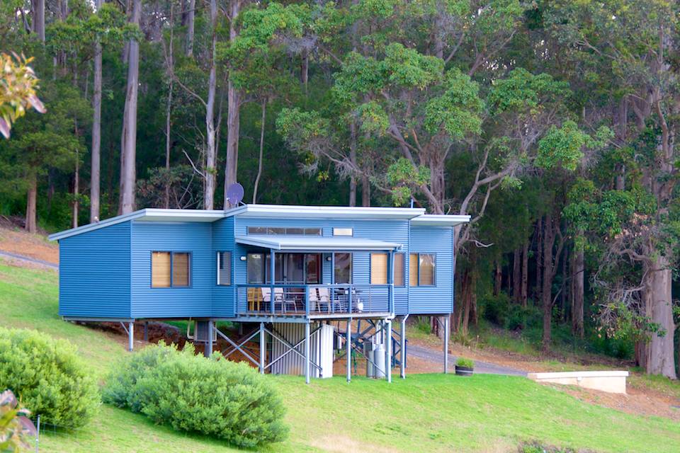 The outside of the Karri chalet with lush green grass and the karri forest behind.