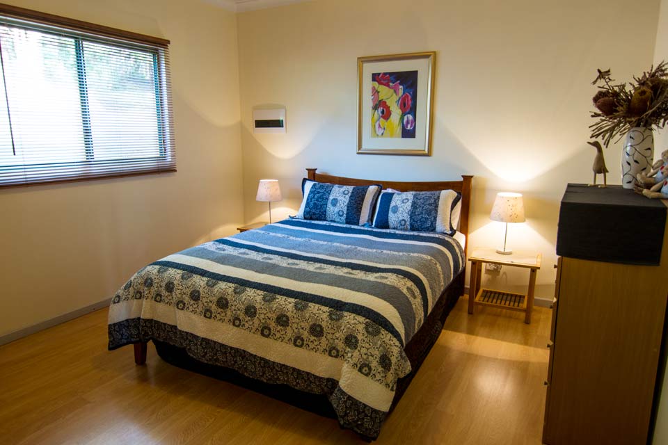 Double bed with a blue bed spread in a room with a wooden floor. 